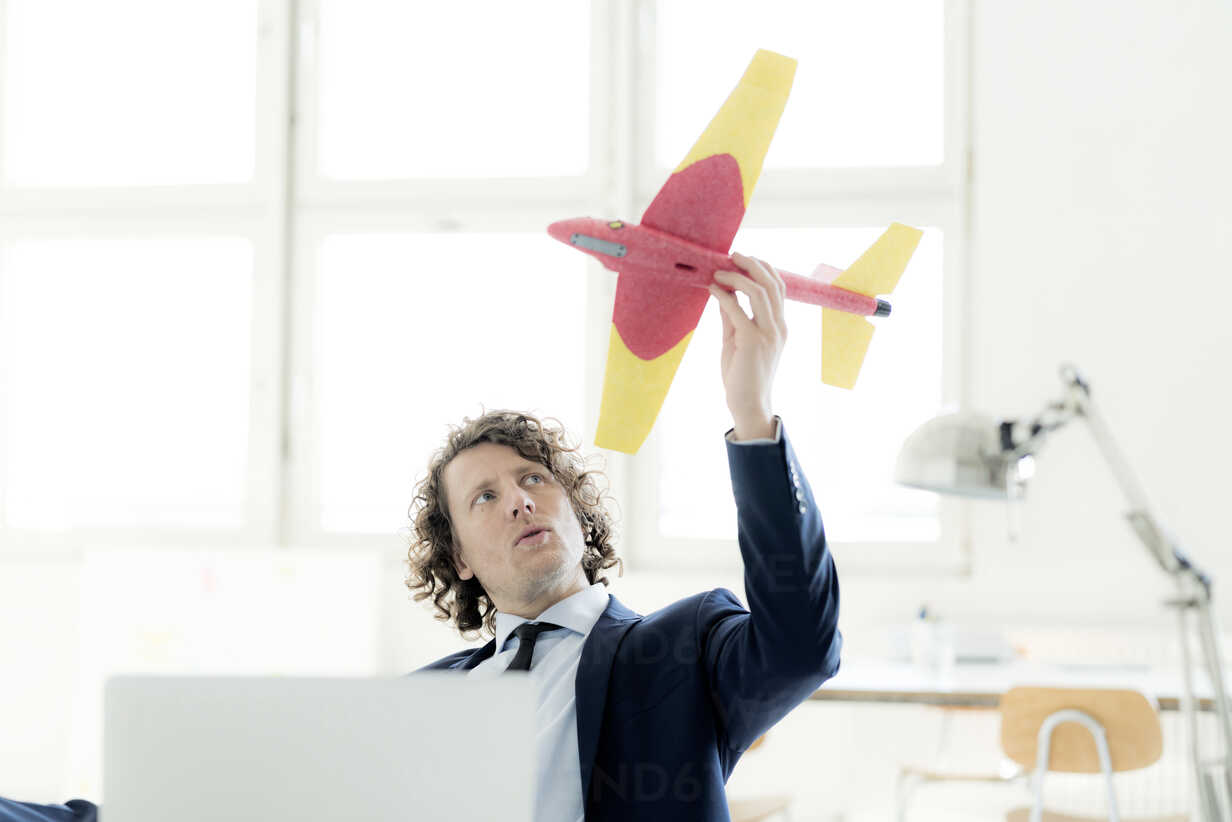 Businessman sitting in his office playing with a toy plane